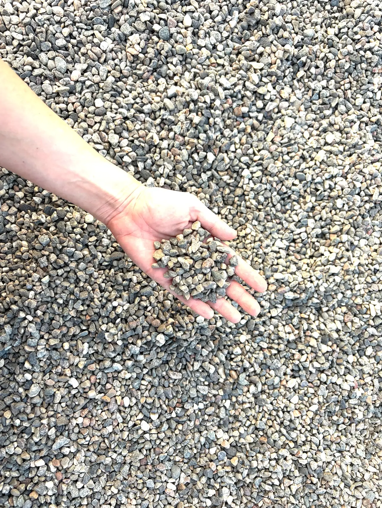 A hand holding a scoop of grey gravel above a heap of it