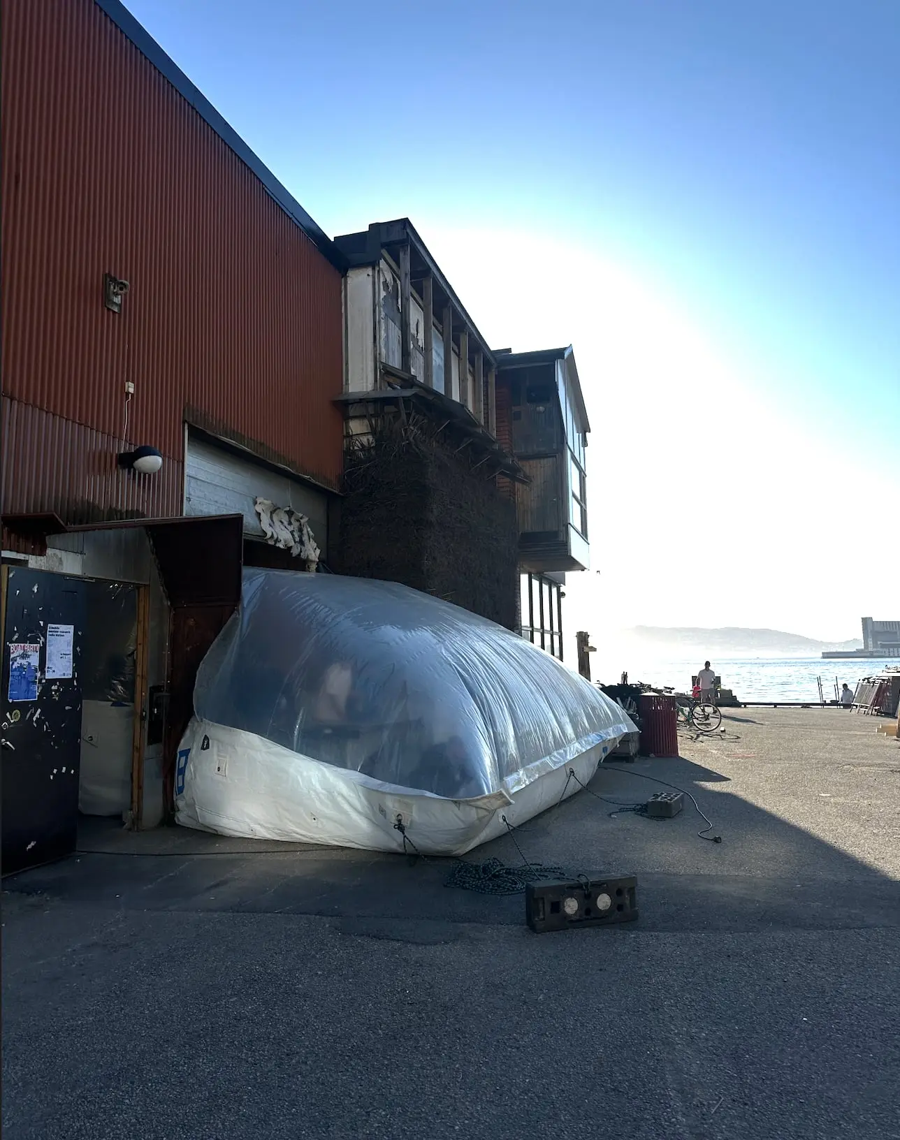 The inflatable squeezed under the gate of a timber building by the harbour, in low sun
