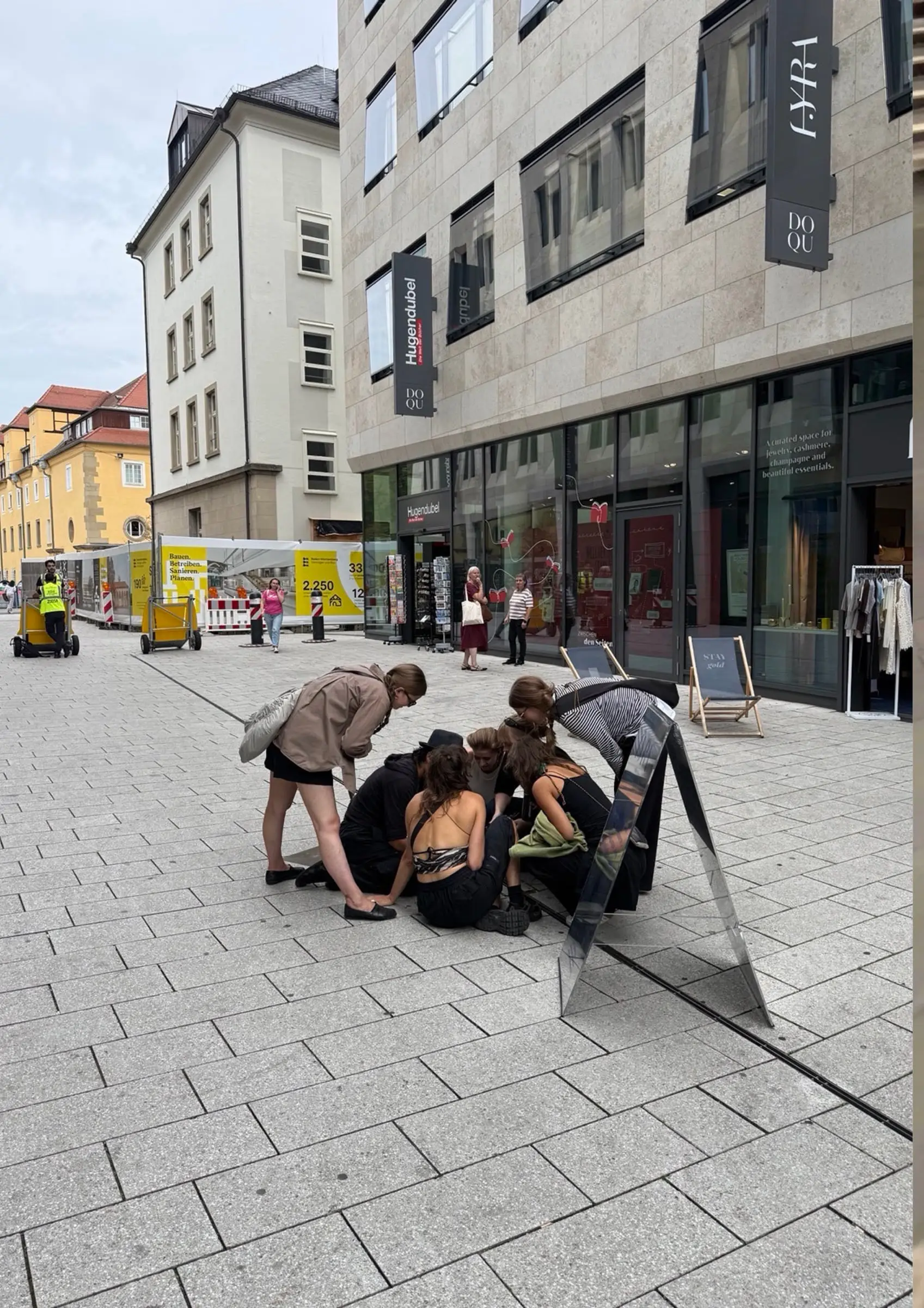 A group of people kneeling around an open manhole in a pedestrian street