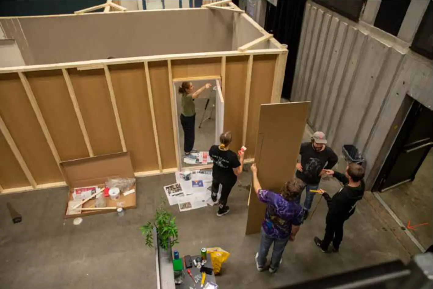 Four people raising and boarding the timber stud walls of the set on the theatre floor