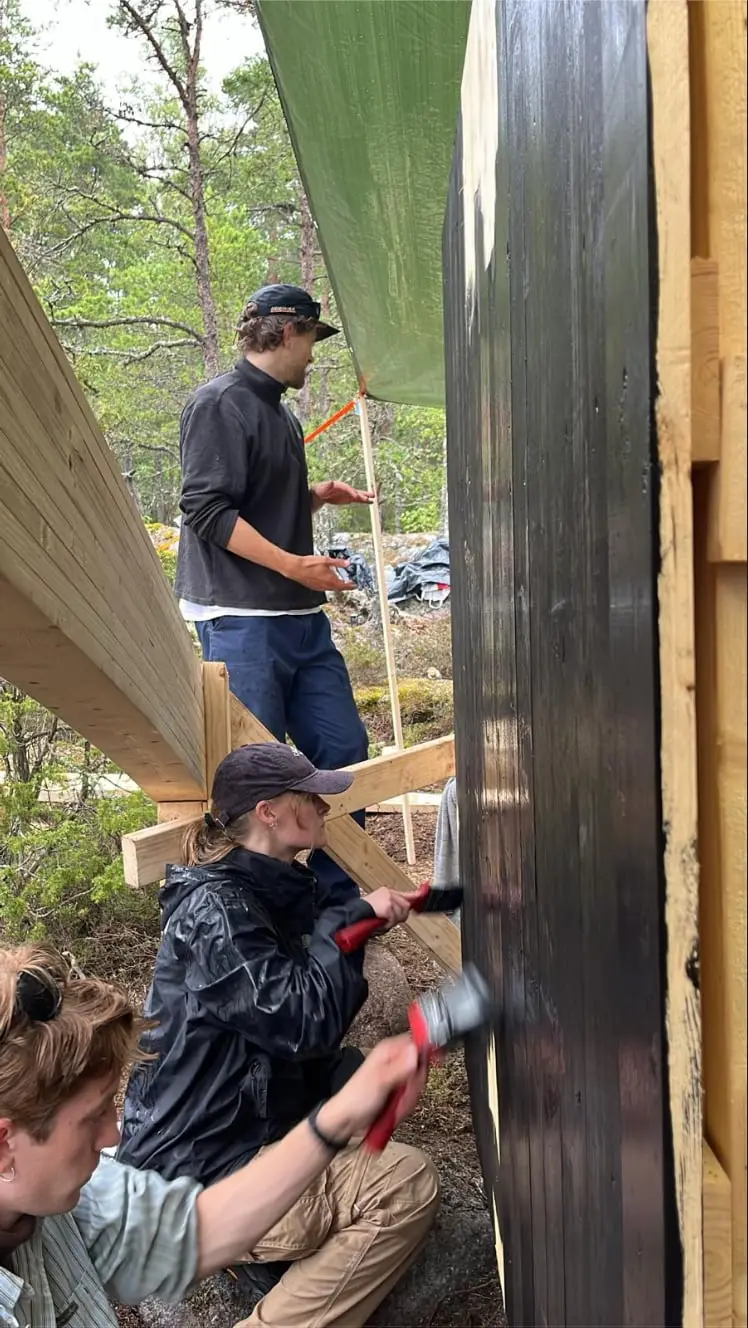 Two students fixing black cladding boards to the shelter wall