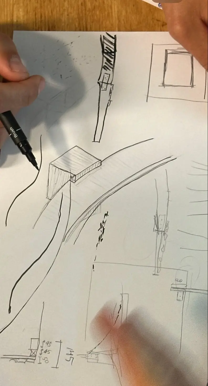 A hand sketching the shelter and the curving bridge in pen