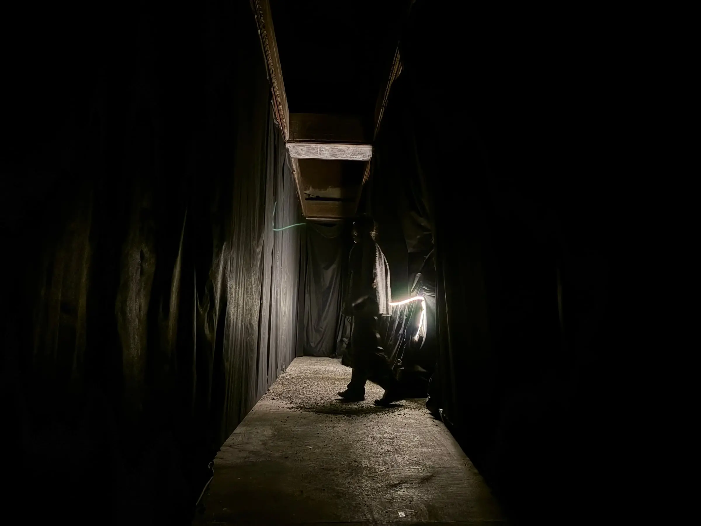 A long dark corridor of black fabric, a strip of light along one wall and a visitor far down it