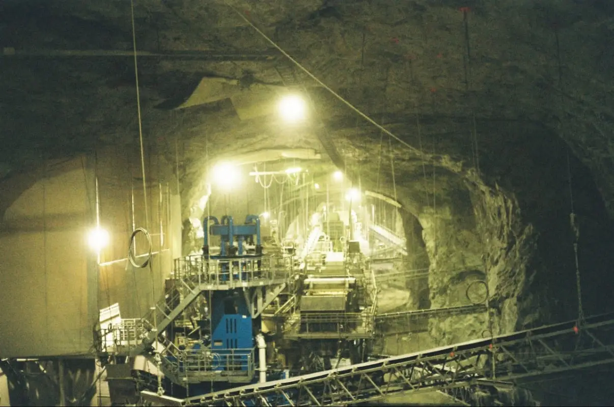 A crushing plant of steel stairs and conveyors lit yellow inside a rock cavern