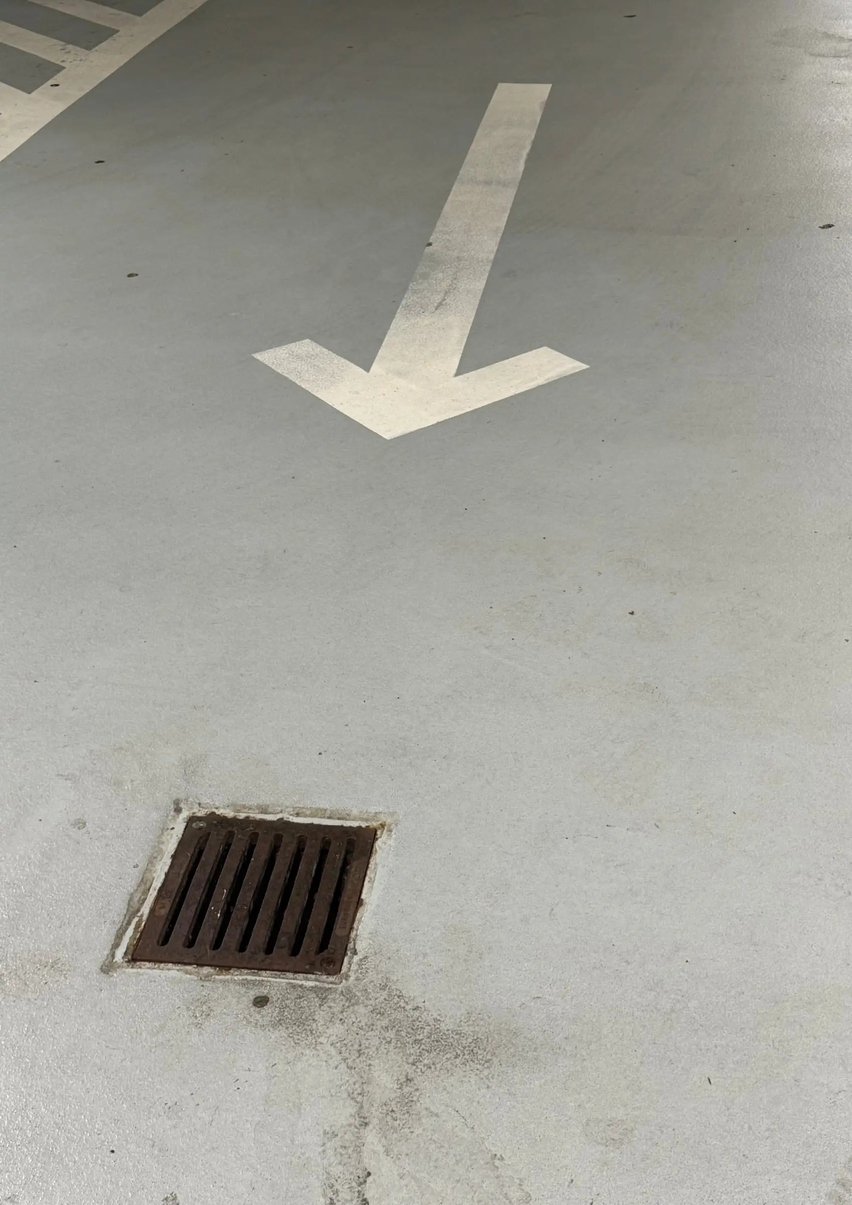 A road arrow painted on asphalt, pointing down at a drain