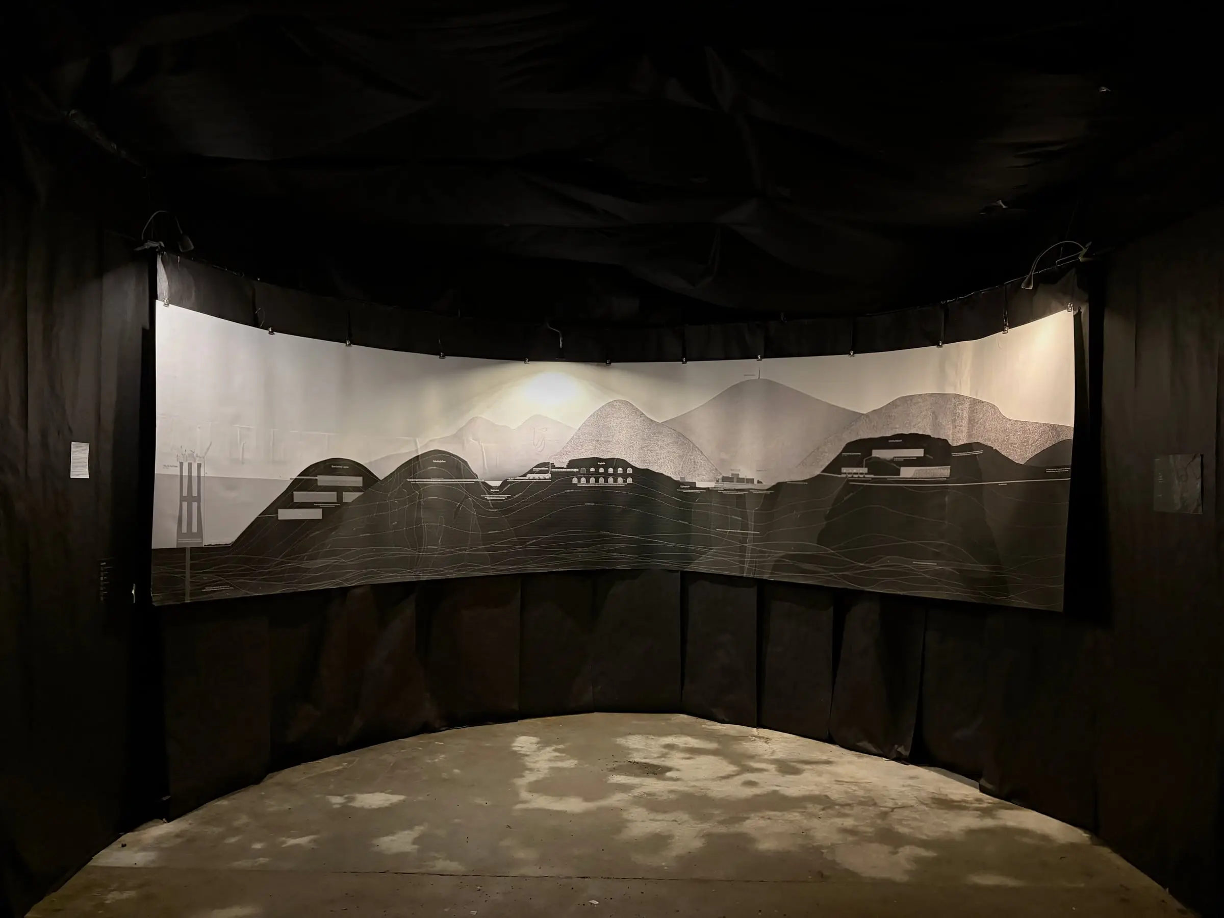 The printed landscape curving around the drawing room, above a black fabric wall and a pale floor