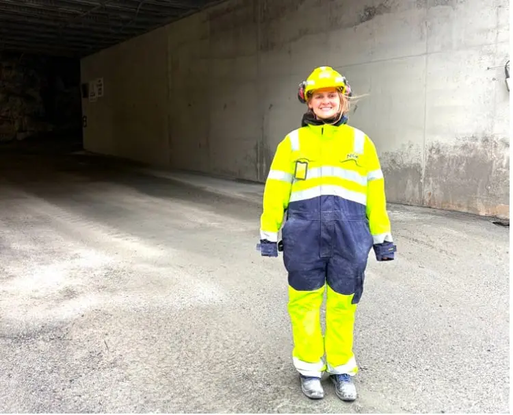 Frida in a hard hat and high-visibility overalls standing in a concrete tunnel