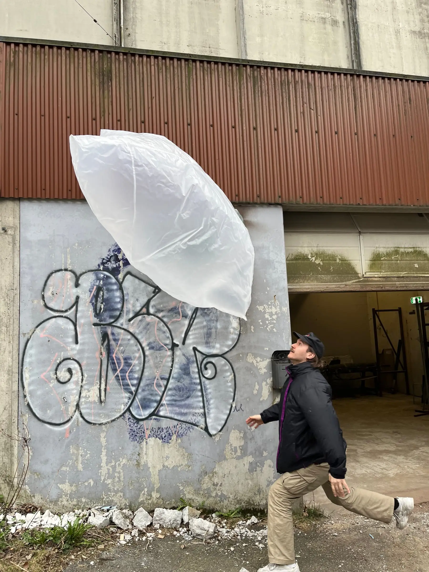 A small plastic bag test blowing up against a graffiti-covered wall while a student lies on the ground beside it