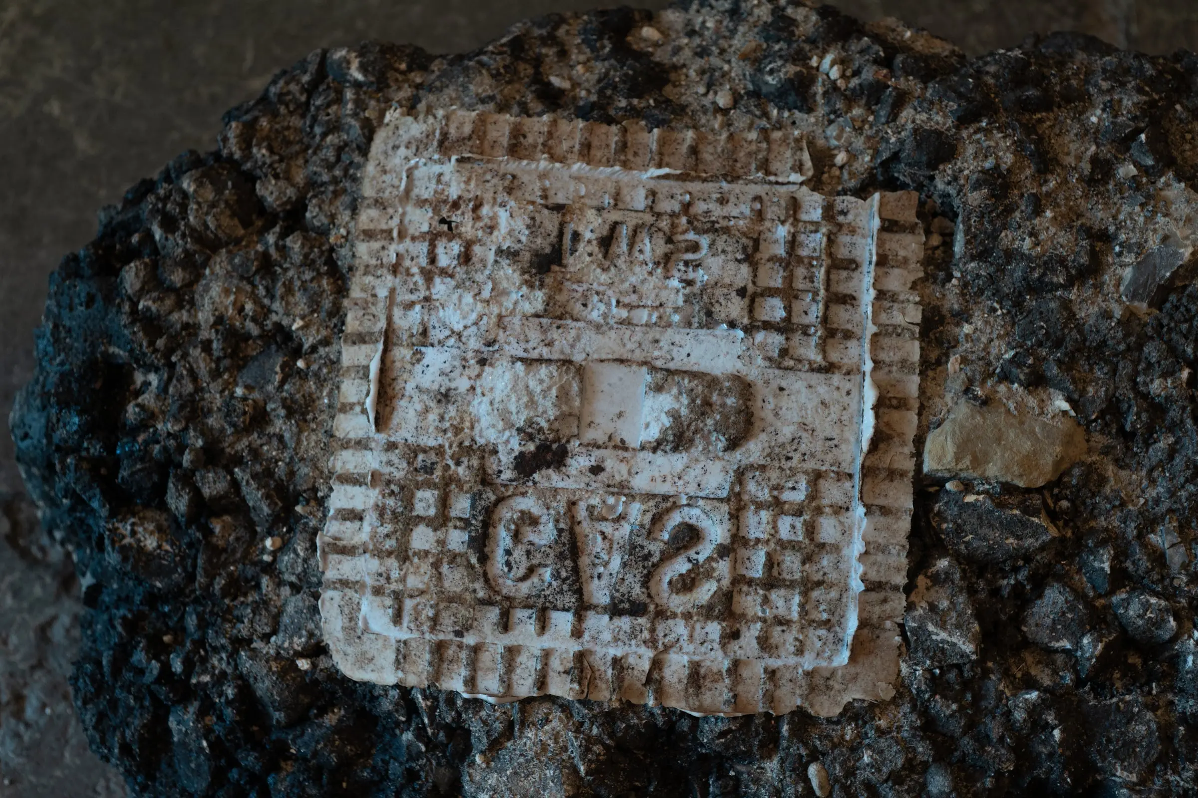 A white cast imprint of a manhole cover lying on dark gravel