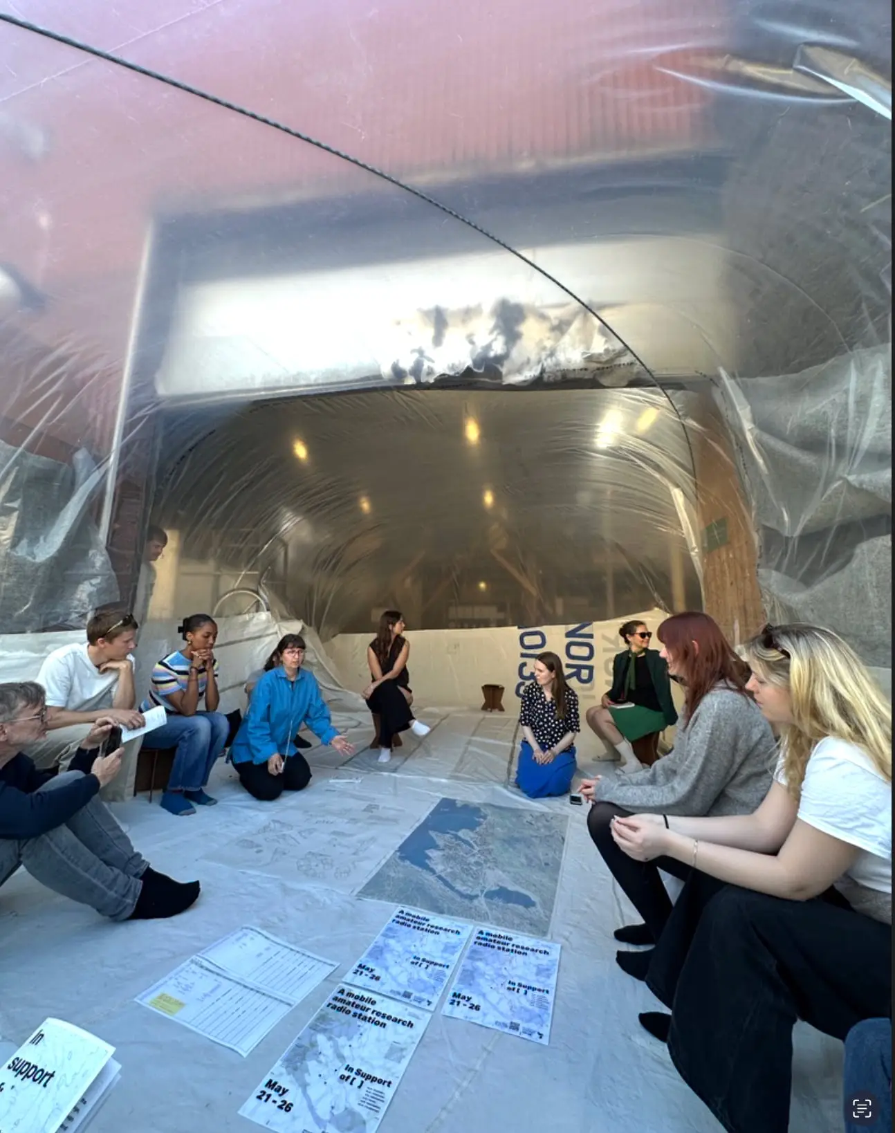 People sitting on the floor inside the inflatable, the plastic roof glowing overhead, papers laid out between them