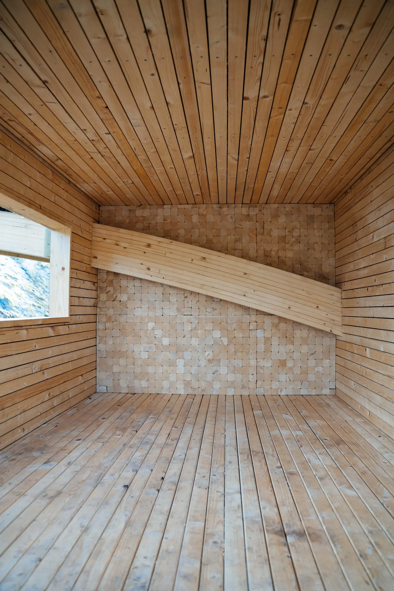 Timber interior of the shelter with a window on one side and a sloping plank wall at the back