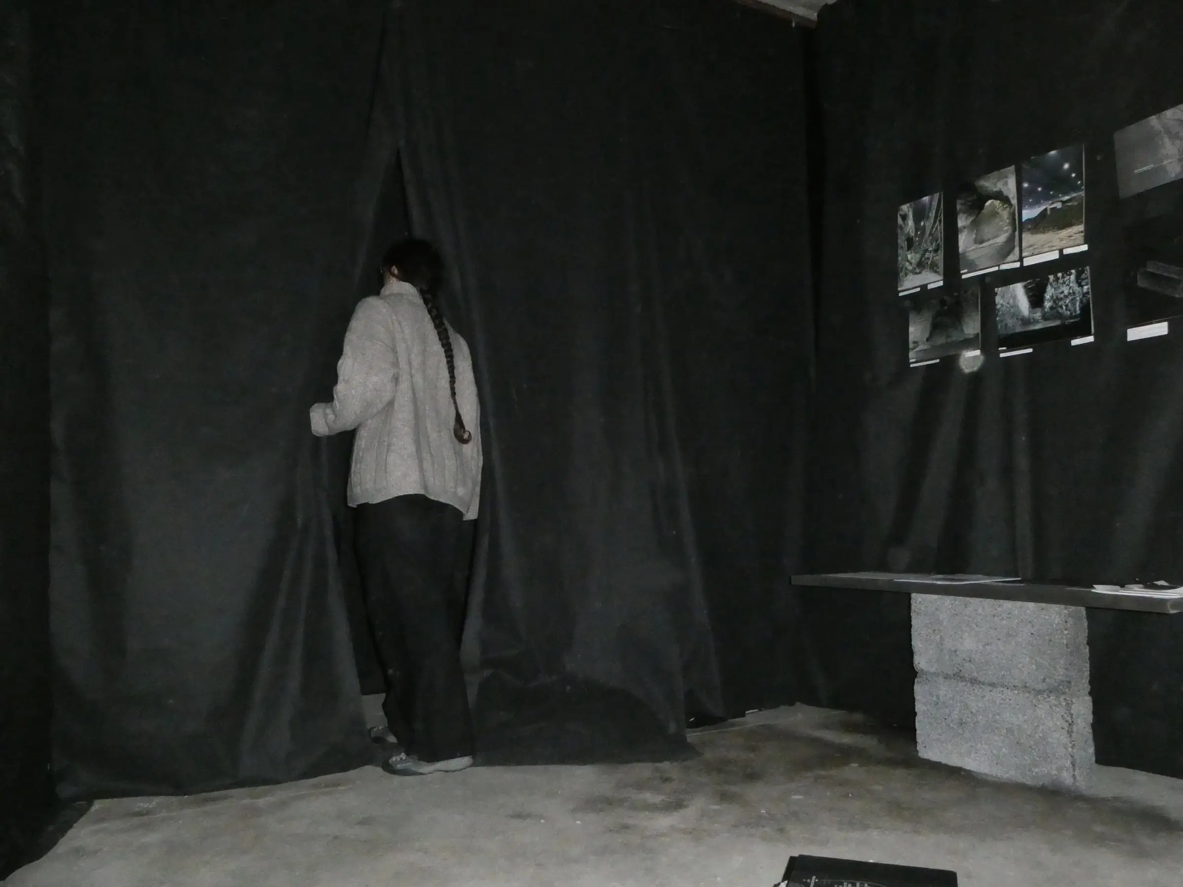 A visitor parting black curtains to step through, photographs of the quarry on the wall beside