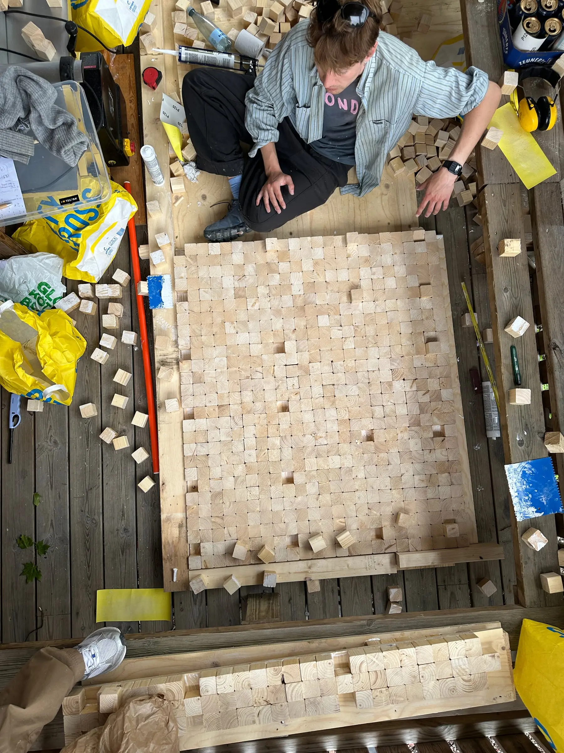 Seen from above, someone fitting end-grain blocks into a timber frame on the ground