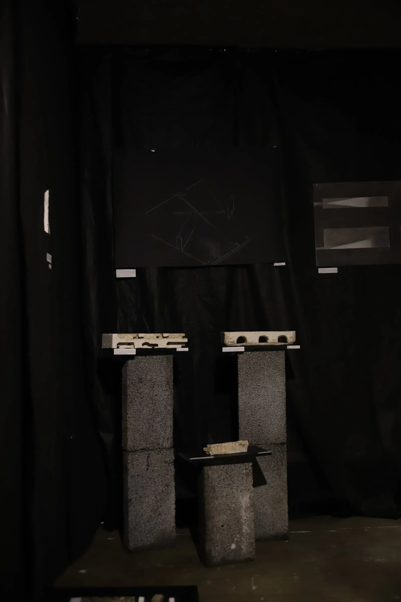 Models of grey stone blocks and small structures on dark plinths against black fabric