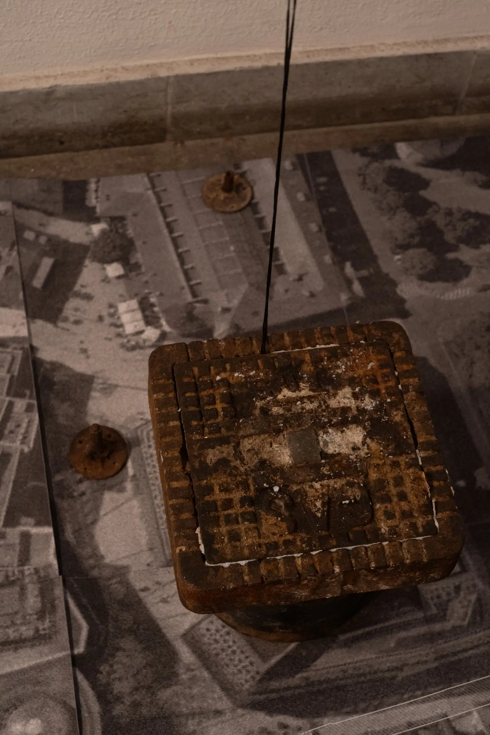 A small square timber model hanging just above a printed aerial photograph of Stuttgart