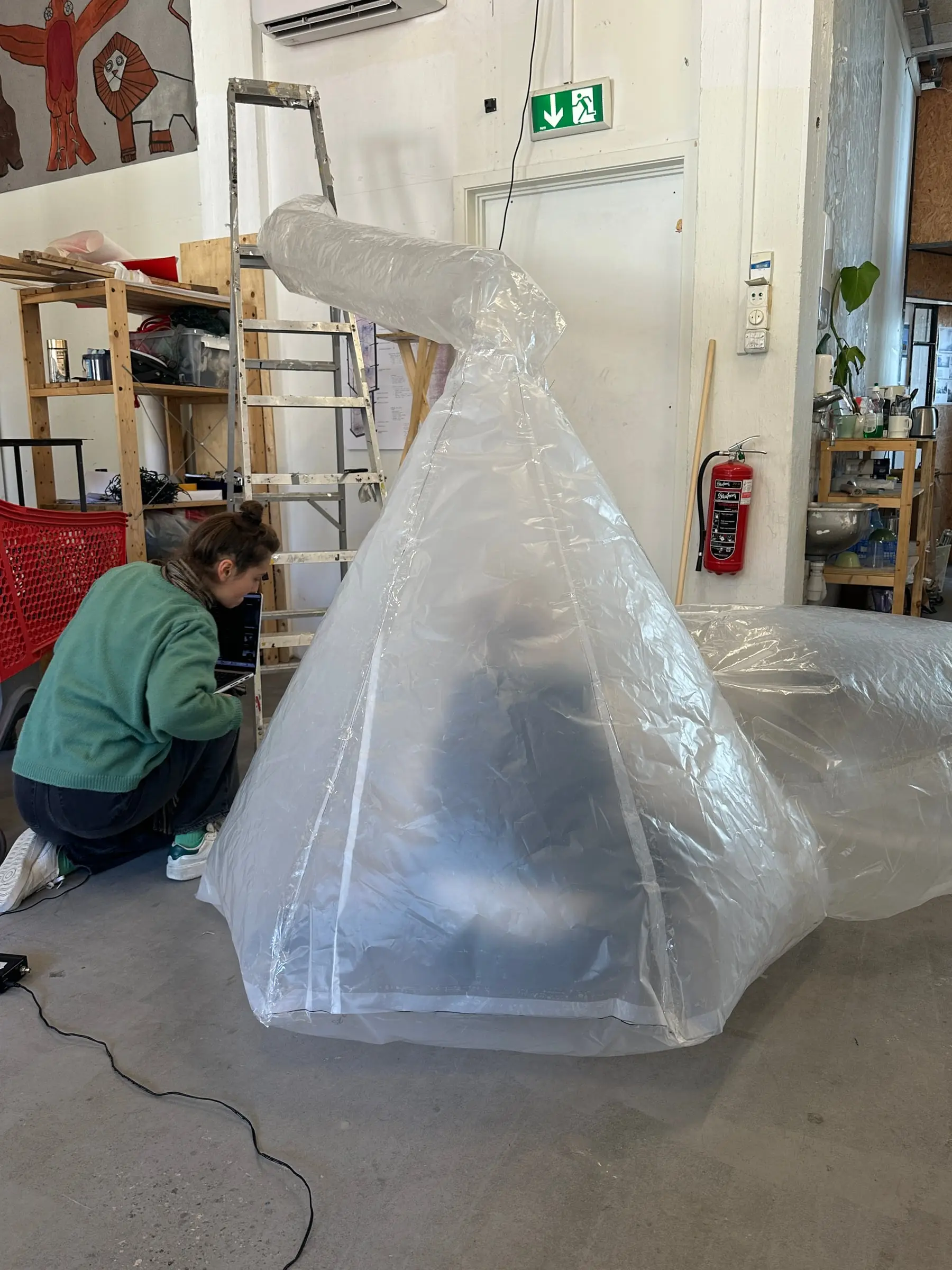 A tall plastic test inflating on a workshop floor, a student crouched beside it