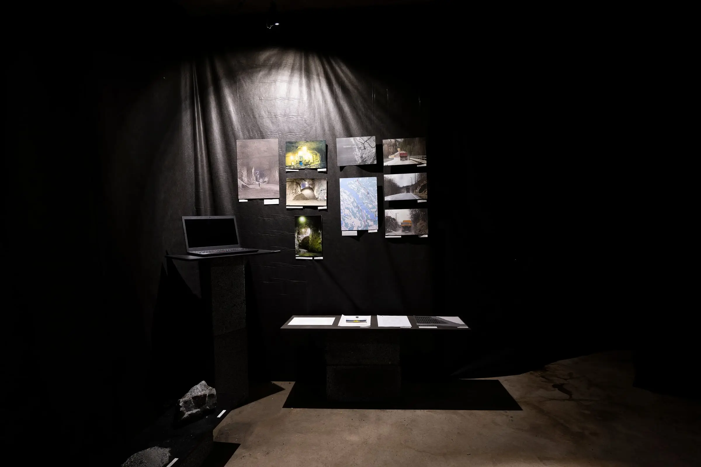 A laptop on a stand and photographs pinned to black fabric above a low table of papers