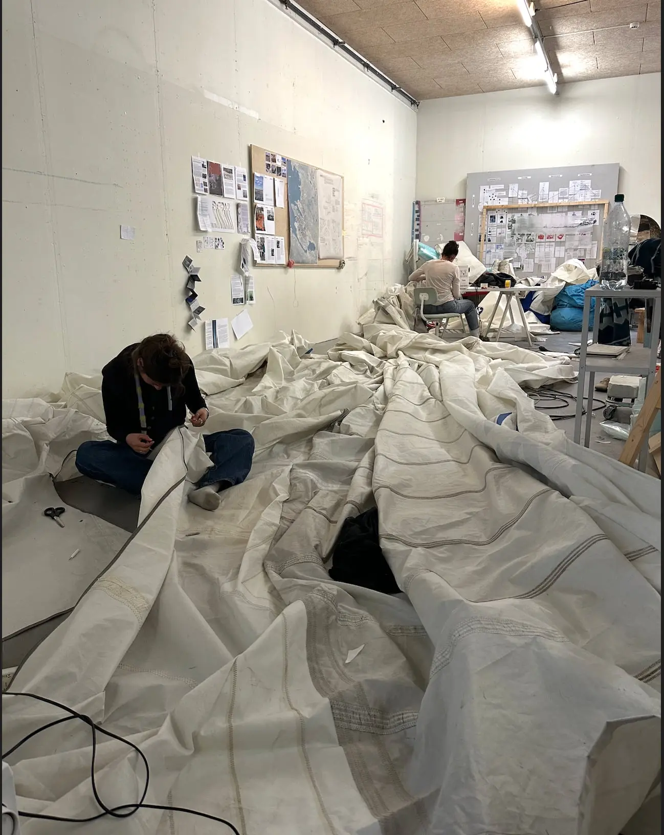 A student sitting among folds of sail fabric, joining the seams