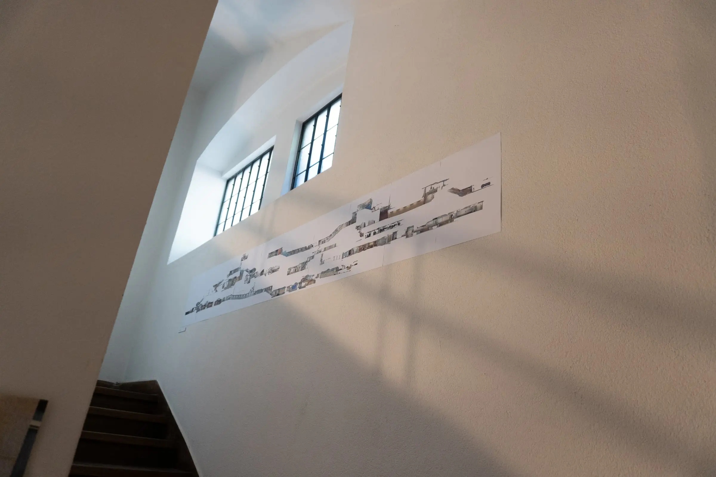 A long printed section mounted high on the stairwell wall under two windows