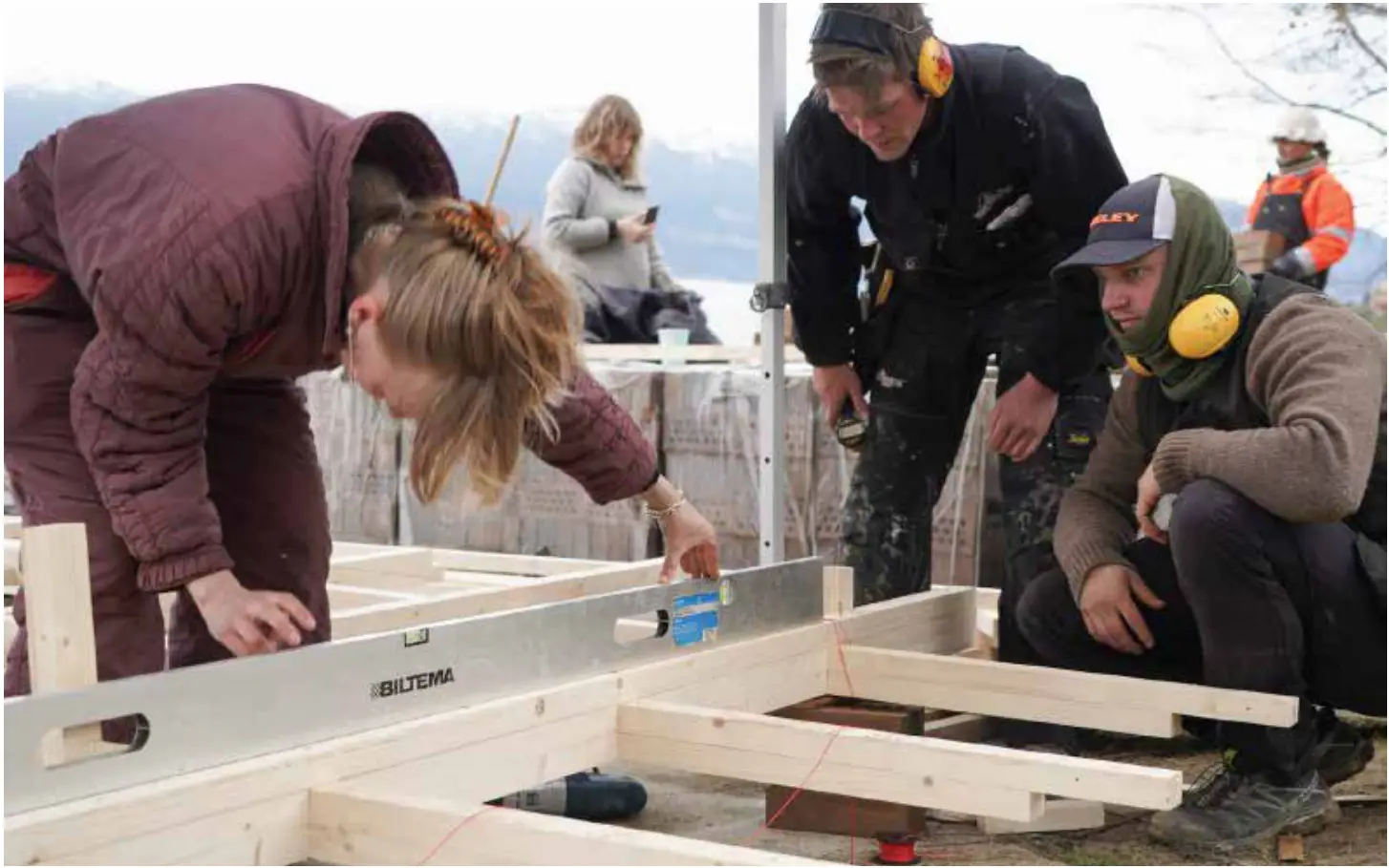 Students levelling the timber sole plates on site, in coats and ear defenders