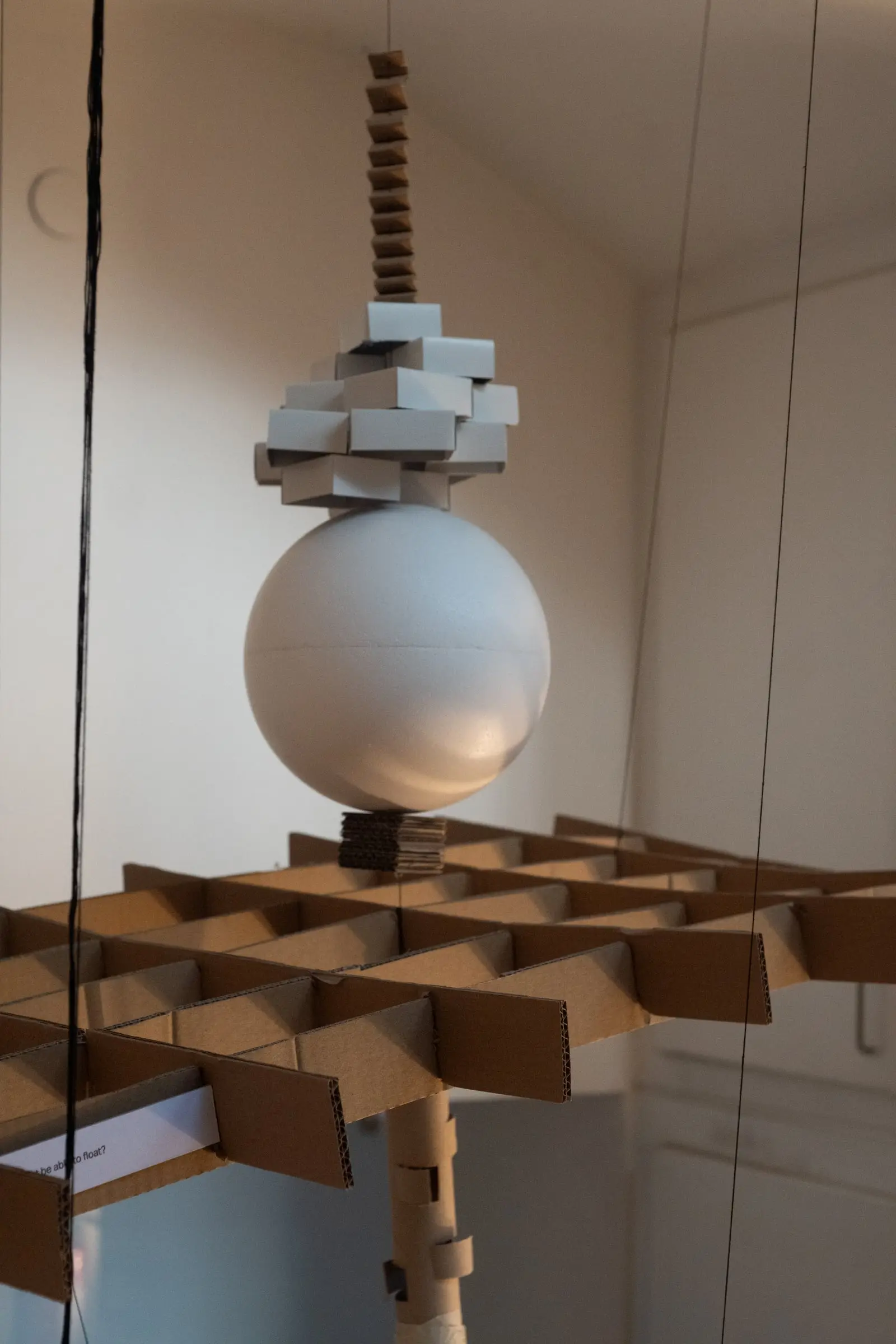 A stack of grey blocks and a white sphere hanging under a zigzag cardboard strip