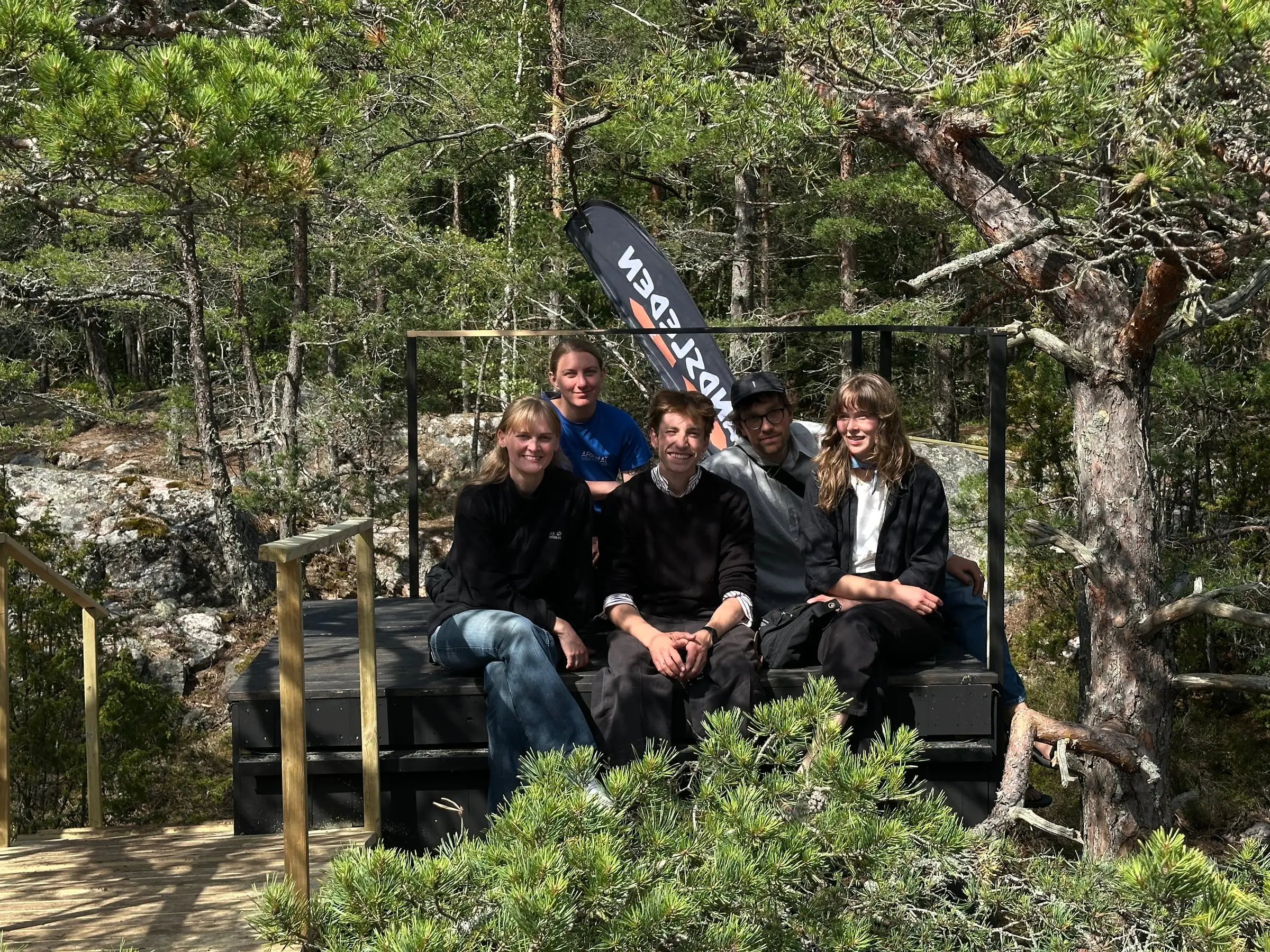 The five team members sitting together on the finished shelter, an ARKNAT flag behind them