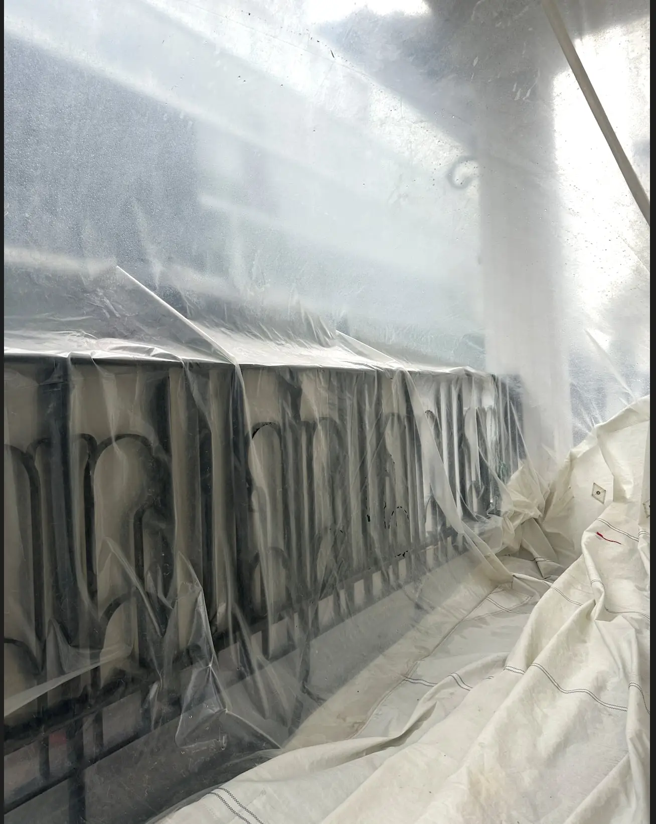 Close view of the plastic pressing against the gate, lettering on the wall seen through it