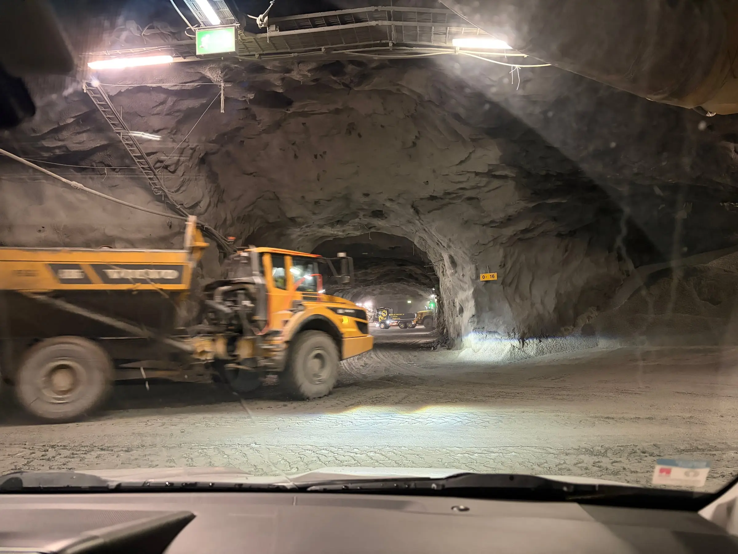 A dump truck driving through a lit hall blasted out of the rock