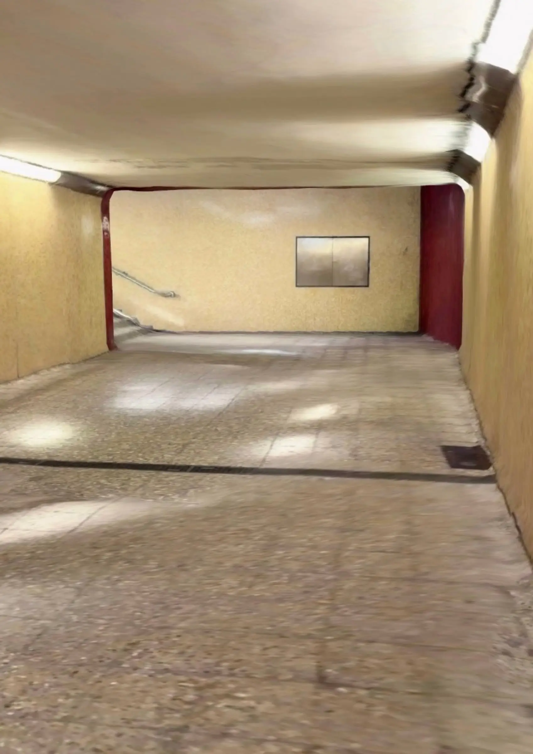 A pale underground passage with a red doorway and a framed picture at the far end